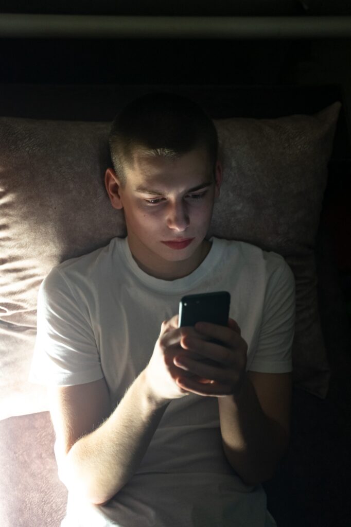 teen lies on bed looking at phone before bedtime