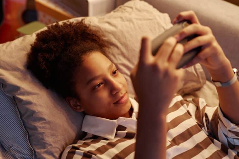 Teen Black Girl Using Smartphone Lying on Bed