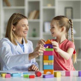 Play Therapy. Little Girl And Child Development Specialist Playing Wooden Bricks Together